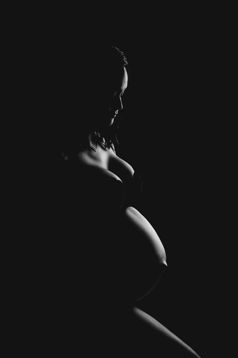 Boise modern maternity — dramatic low-key black-and-white profile, single light revealing the silhouette